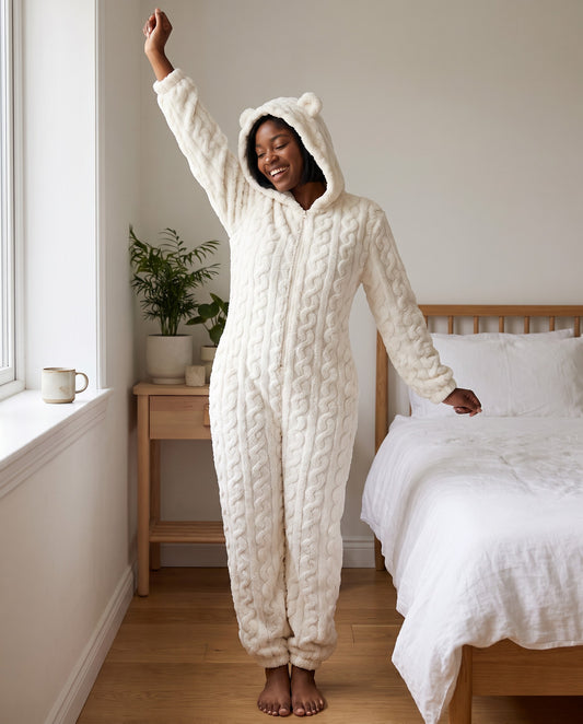 Woman stretching in a bright bedroom in the TEDDY Cozy Bear Onesie in White, hood up with bear ears